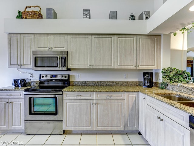 kitchen with light stone counters, light tile patterned floors, stainless steel appliances, and a sink