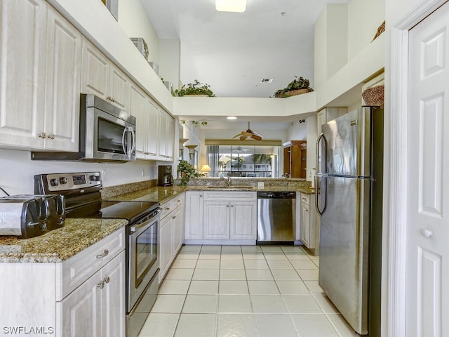 kitchen with light stone countertops, light tile patterned floors, appliances with stainless steel finishes, white cabinetry, and a sink