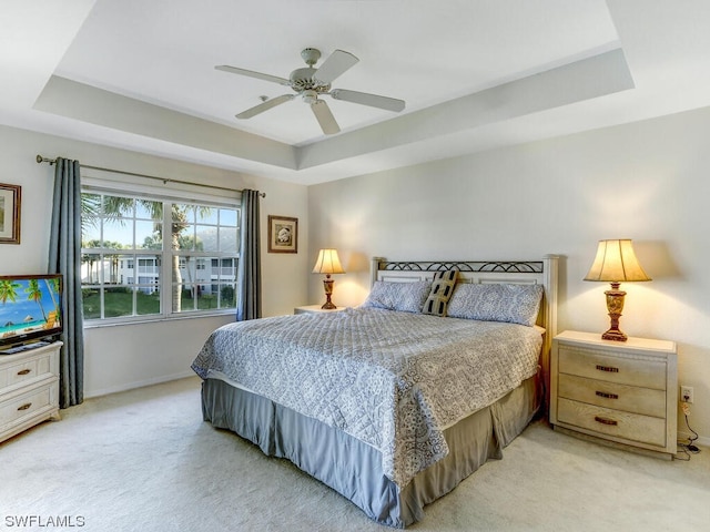 bedroom with light colored carpet, baseboards, a raised ceiling, and a ceiling fan