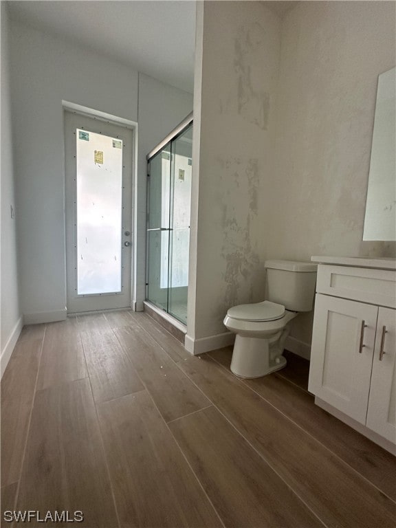 bathroom with hardwood / wood-style flooring, vanity, a shower with door, and toilet