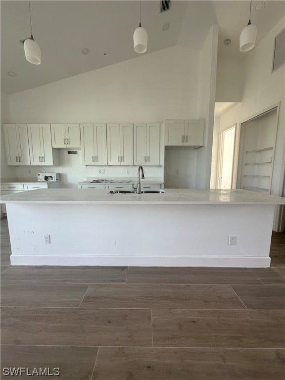 kitchen featuring high vaulted ceiling, a center island with sink, hanging light fixtures, and white cabinetry