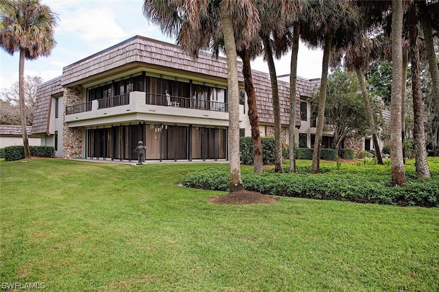 rear view of property featuring a balcony and a yard