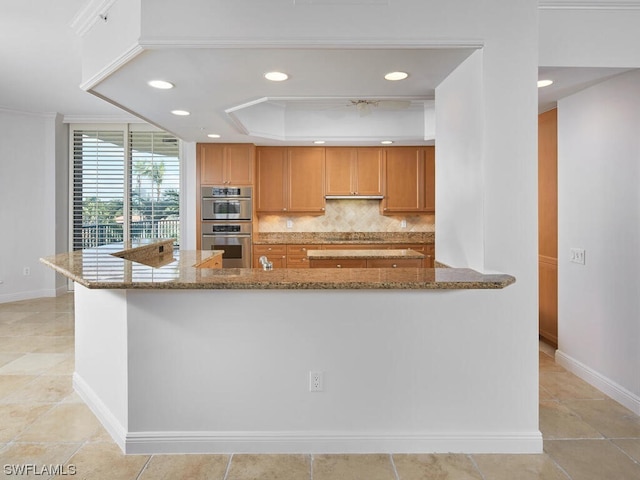 kitchen with backsplash, double oven, light tile flooring, a tray ceiling, and stone counters