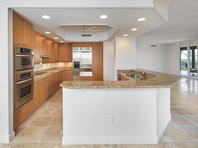 kitchen featuring ceiling fan, light stone counters, a raised ceiling, appliances with stainless steel finishes, and light tile flooring