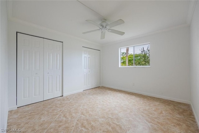 unfurnished bedroom featuring light tile patterned floors, a ceiling fan, baseboards, multiple closets, and crown molding