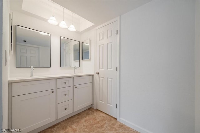 full bath featuring a raised ceiling, a sink, baseboards, and double vanity