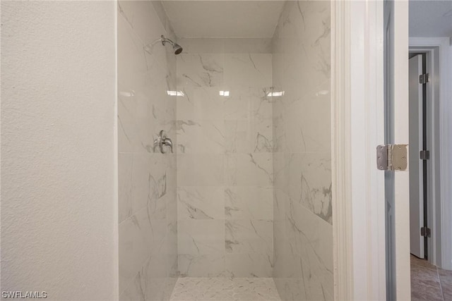 bathroom with a marble finish shower and a textured wall