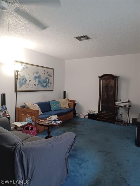 carpeted living room featuring ceiling fan and a textured ceiling