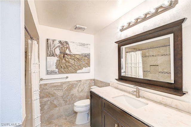 bathroom featuring vanity, toilet, and tile walls