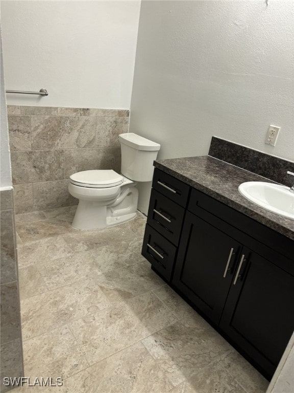 bathroom with vanity, toilet, and tile walls