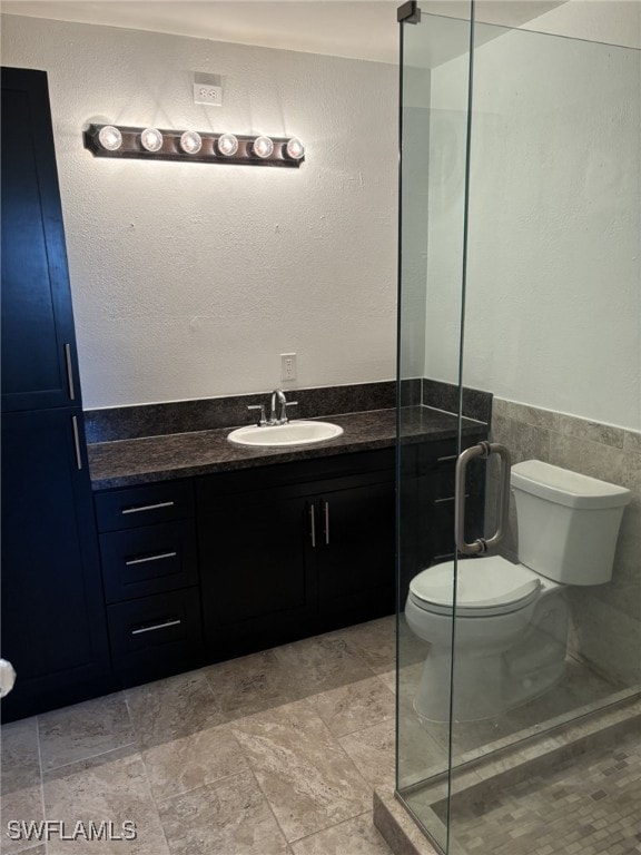 bathroom with a shower with door, vanity, tile walls, and toilet