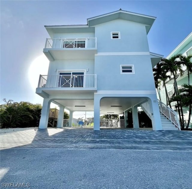 view of front of home with a carport, stucco siding, a balcony, and stairs