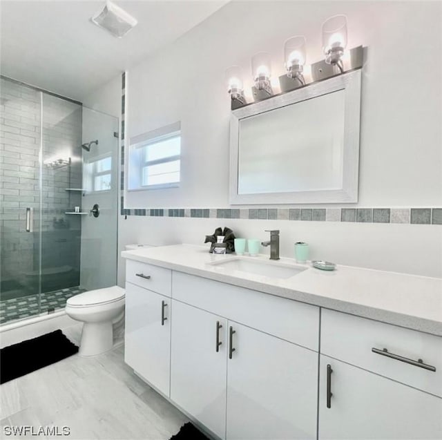 bathroom featuring toilet, a stall shower, vanity, and tile walls