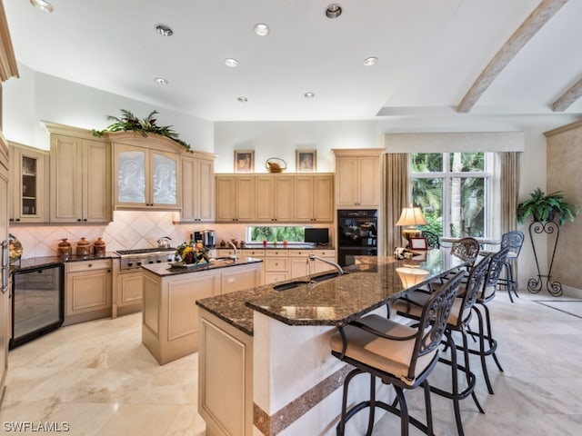 kitchen featuring sink, wine cooler, double oven, a kitchen island with sink, and light brown cabinetry