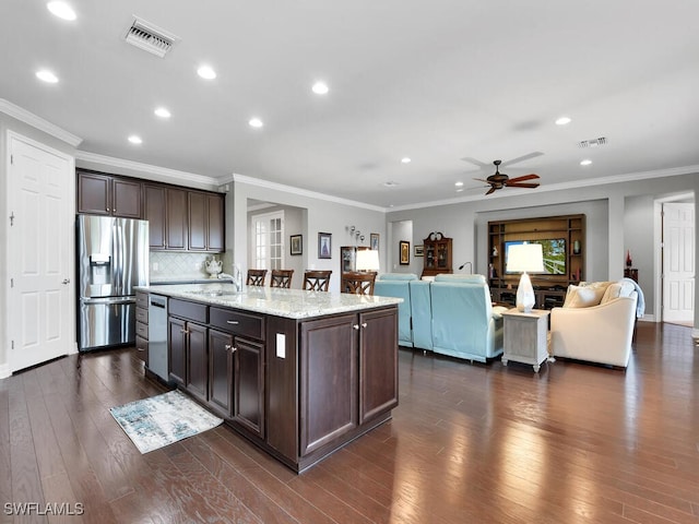 kitchen with appliances with stainless steel finishes, tasteful backsplash, ornamental molding, a kitchen island with sink, and dark brown cabinets