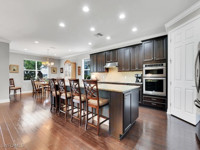 kitchen with pendant lighting, a breakfast bar, dark brown cabinetry, ornamental molding, and a kitchen island