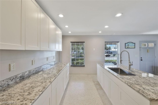 kitchen with white cabinetry, sink, and light stone countertops