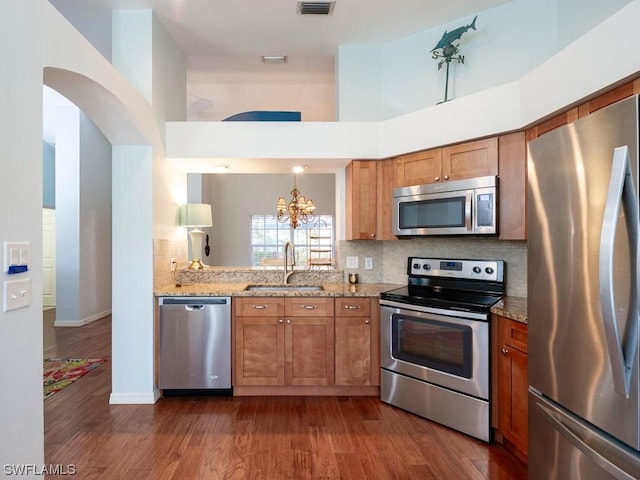 kitchen with sink, backsplash, a towering ceiling, stainless steel appliances, and light stone countertops