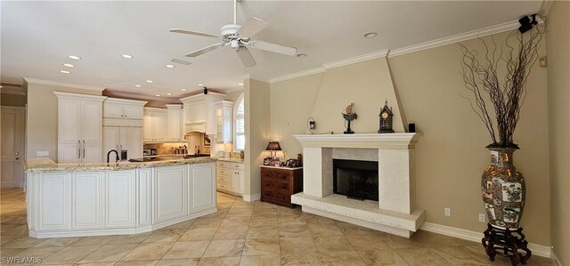 kitchen featuring white cabinetry, a high end fireplace, light stone countertops, ceiling fan, and crown molding