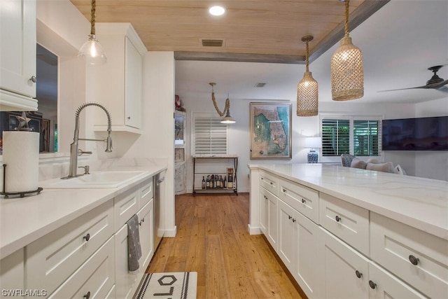 kitchen featuring light wood-type flooring, white cabinets, a sink, and hanging light fixtures