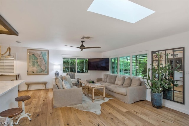 living room featuring light wood-style flooring, a skylight, visible vents, and a ceiling fan