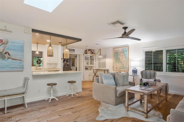 living area with ceiling fan, a skylight, visible vents, baseboards, and light wood-type flooring