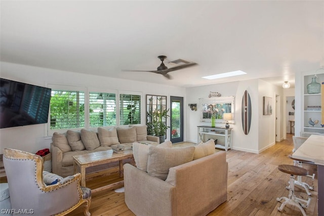 living room featuring a healthy amount of sunlight, a skylight, light wood-style flooring, and a ceiling fan