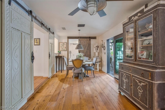 dining room with a barn door, light wood-type flooring, visible vents, and a ceiling fan