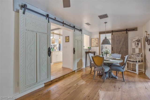 dining space with a barn door, light wood-style flooring, and visible vents