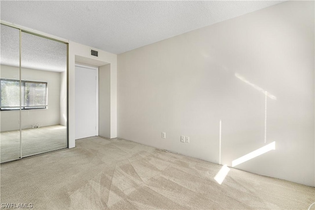 unfurnished bedroom with a textured ceiling, light carpet, and a closet