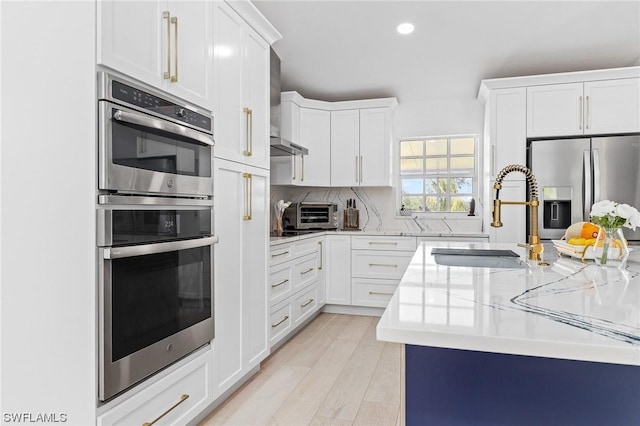 kitchen with white cabinets, sink, light stone countertops, light wood-type flooring, and appliances with stainless steel finishes