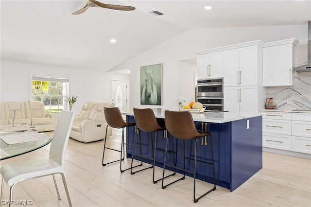 kitchen featuring light hardwood / wood-style flooring, white cabinetry, double oven, and a kitchen island with sink