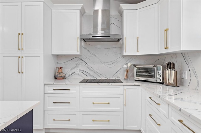 kitchen featuring tasteful backsplash, light stone counters, wall chimney exhaust hood, black electric cooktop, and white cabinets