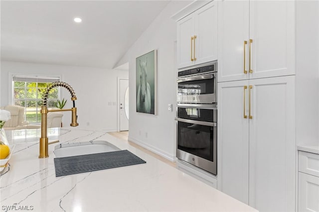 kitchen with white cabinets, light stone countertops, stainless steel double oven, and vaulted ceiling