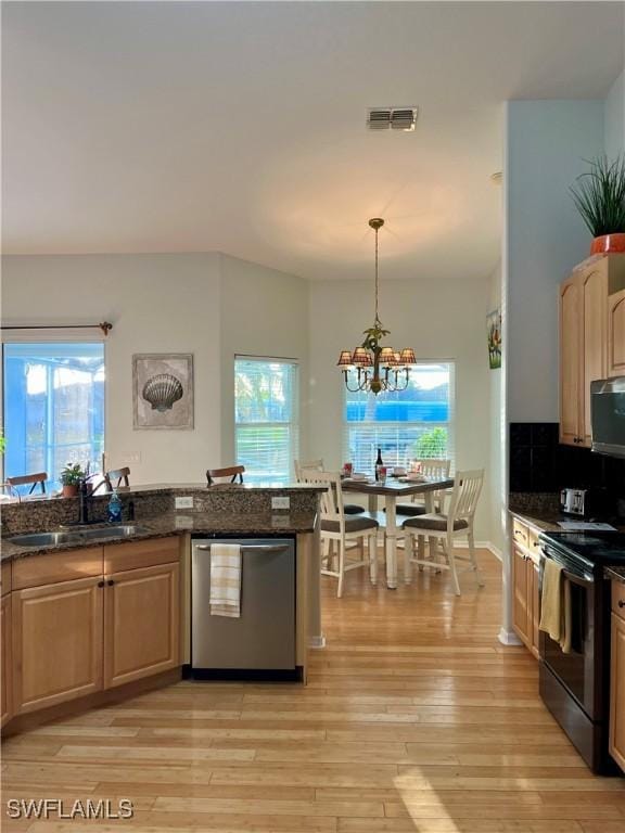 kitchen with appliances with stainless steel finishes, decorative light fixtures, sink, and dark stone countertops