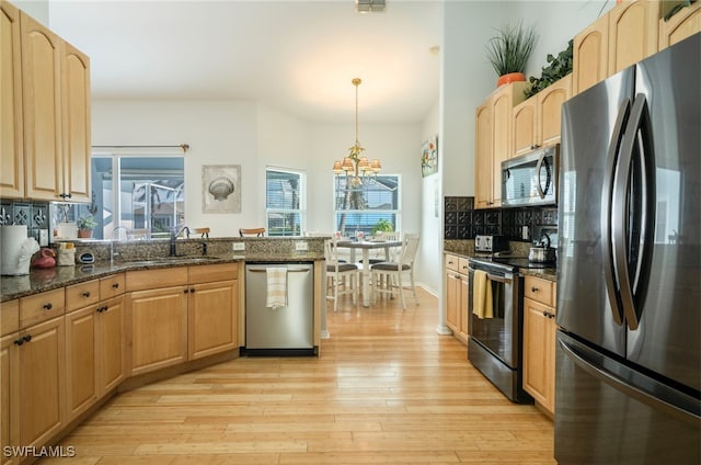 kitchen featuring light wood-type flooring, dark stone counters, decorative light fixtures, stainless steel appliances, and tasteful backsplash