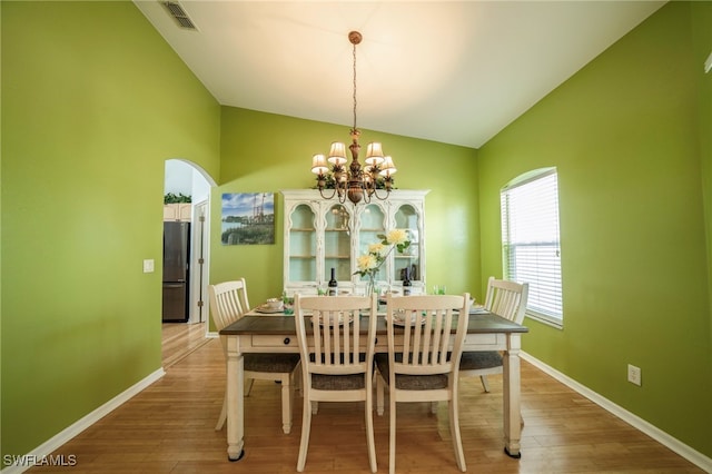 dining space with hardwood / wood-style floors, vaulted ceiling, and a notable chandelier