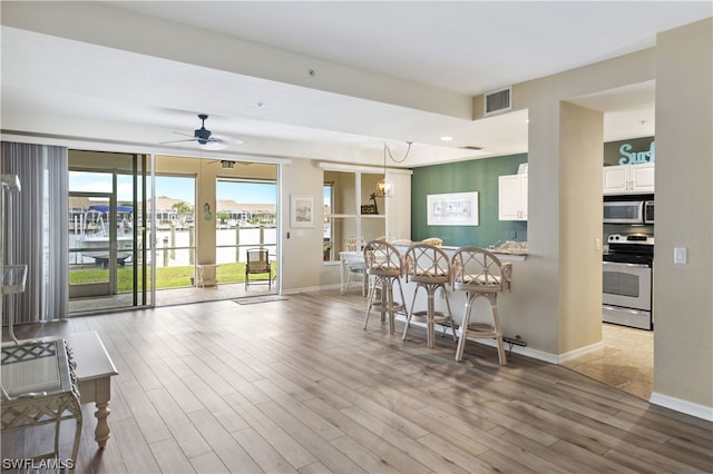 kitchen with hanging light fixtures, ceiling fan with notable chandelier, light wood-type flooring, white cabinets, and stove