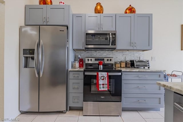 kitchen featuring gray cabinets, light tile patterned floors, stainless steel appliances, and backsplash