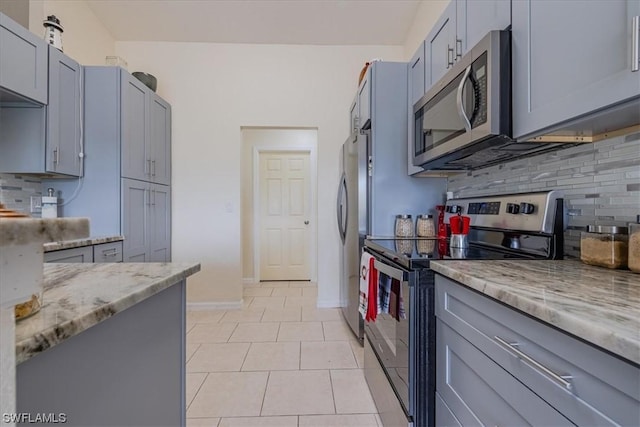 kitchen with appliances with stainless steel finishes, light tile patterned floors, gray cabinets, light stone countertops, and tasteful backsplash