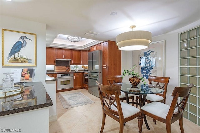 kitchen featuring kitchen peninsula, dark stone counters, stainless steel appliances, a raised ceiling, and light tile patterned floors