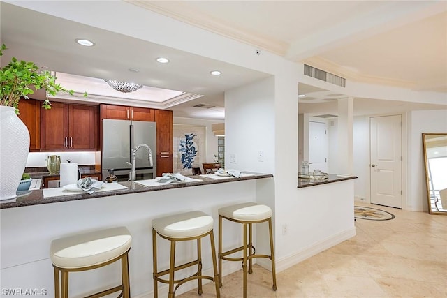 kitchen featuring a kitchen breakfast bar, stainless steel refrigerator, kitchen peninsula, and ornamental molding