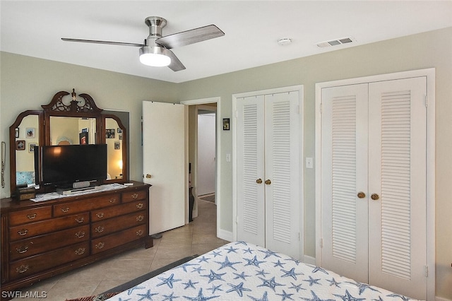 tiled bedroom with ceiling fan and two closets