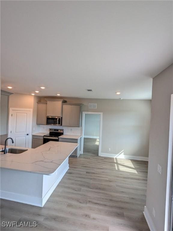 kitchen featuring sink, light stone counters, gray cabinets, stainless steel appliances, and light hardwood / wood-style floors