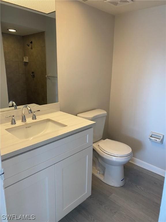 bathroom with vanity, tiled shower, hardwood / wood-style floors, and toilet