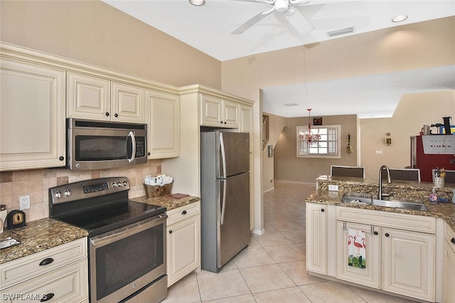 kitchen with dark stone counters, cream cabinets, sink, light tile patterned floors, and appliances with stainless steel finishes