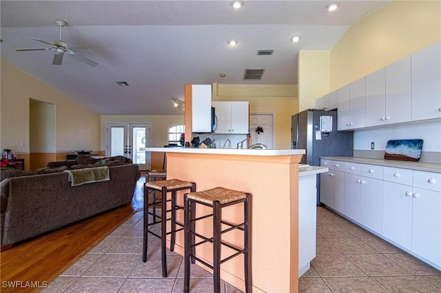 kitchen with vaulted ceiling, light tile patterned floors, white cabinets, a center island, and a breakfast bar area