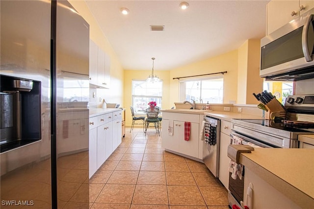 kitchen featuring pendant lighting, lofted ceiling, white cabinets, light tile patterned floors, and appliances with stainless steel finishes