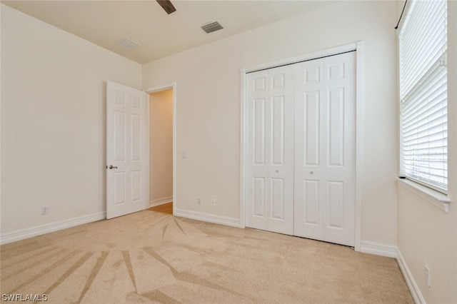 unfurnished bedroom featuring a closet, light colored carpet, and ceiling fan