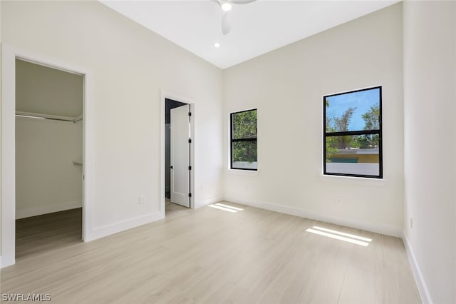 unfurnished bedroom with ceiling fan, a walk in closet, light hardwood / wood-style floors, and a closet